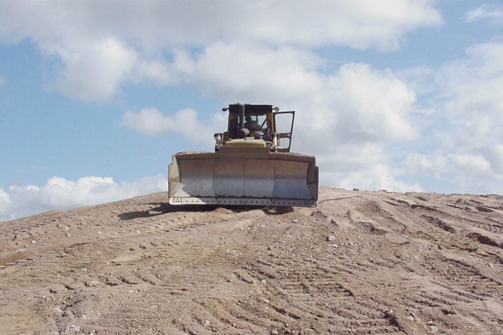 En arbetsmaskin kör fram över en stor hög med sand/grus